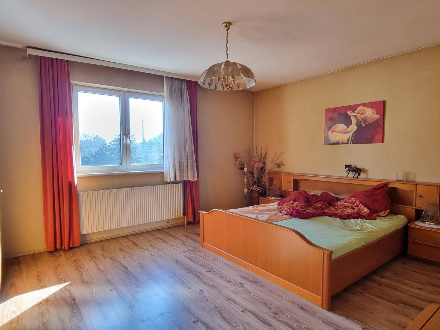 Schlafzimmer mit Holzbett, Laminatboden und großem Fenster mit grüner Aussicht.