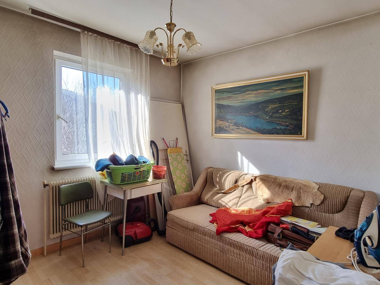 Helles Zimmer mit Sofa, Laminatboden und großem Fenster.
