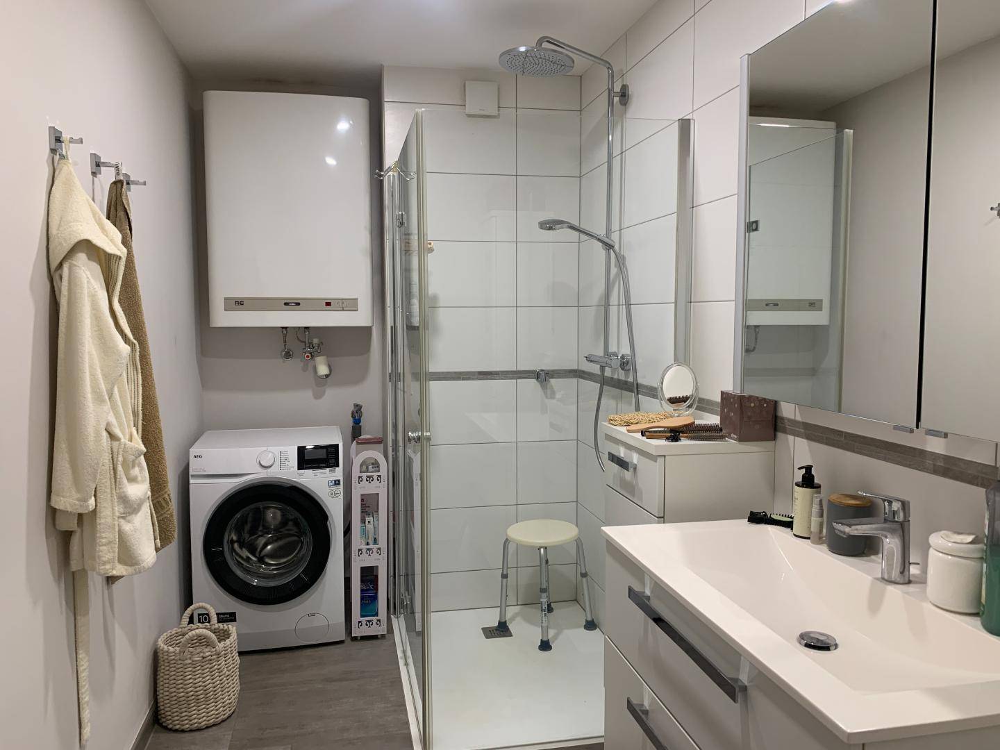 Badezimmer mit Duschkabine, Waschmaschine und Warmwasserbereiter an der Wand.