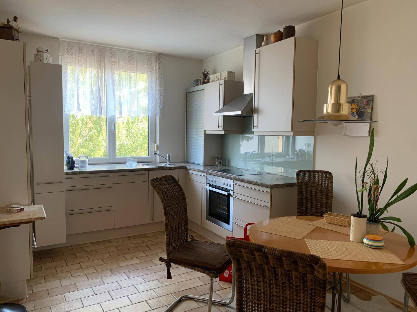 Funktionale Küche mit hellen Einbauschränken, Essbereich und großem Fenster mit Blick ins Grüne.
