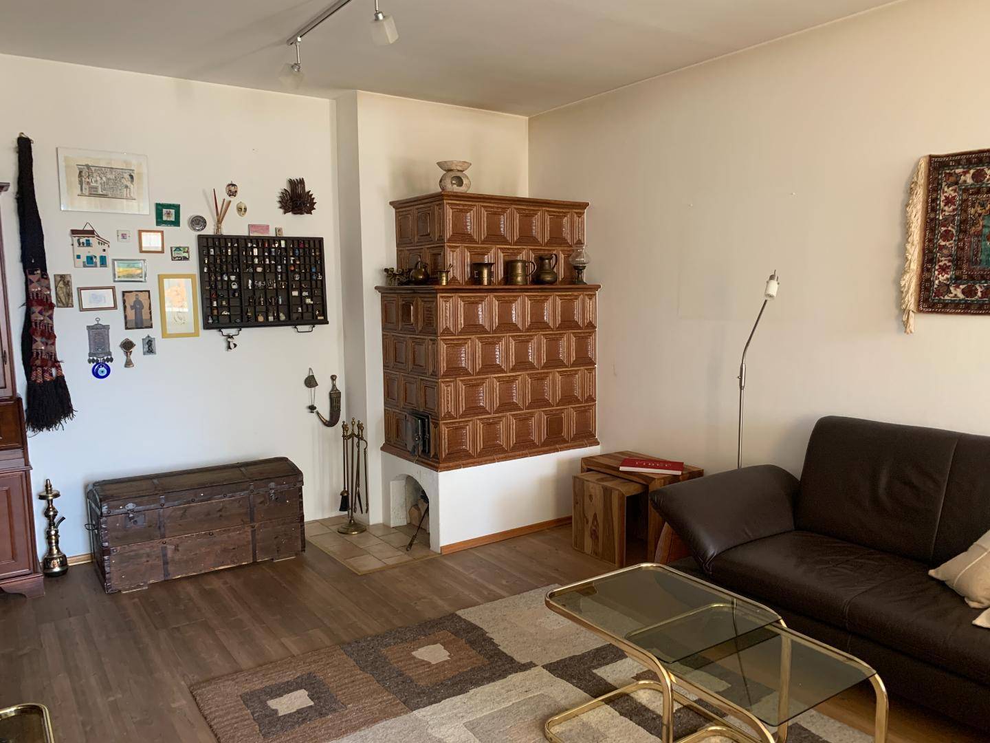 Geräumiges Wohnzimmer mit traditionellem Kachelofen als Blickfang und dunklem Holzfußboden.