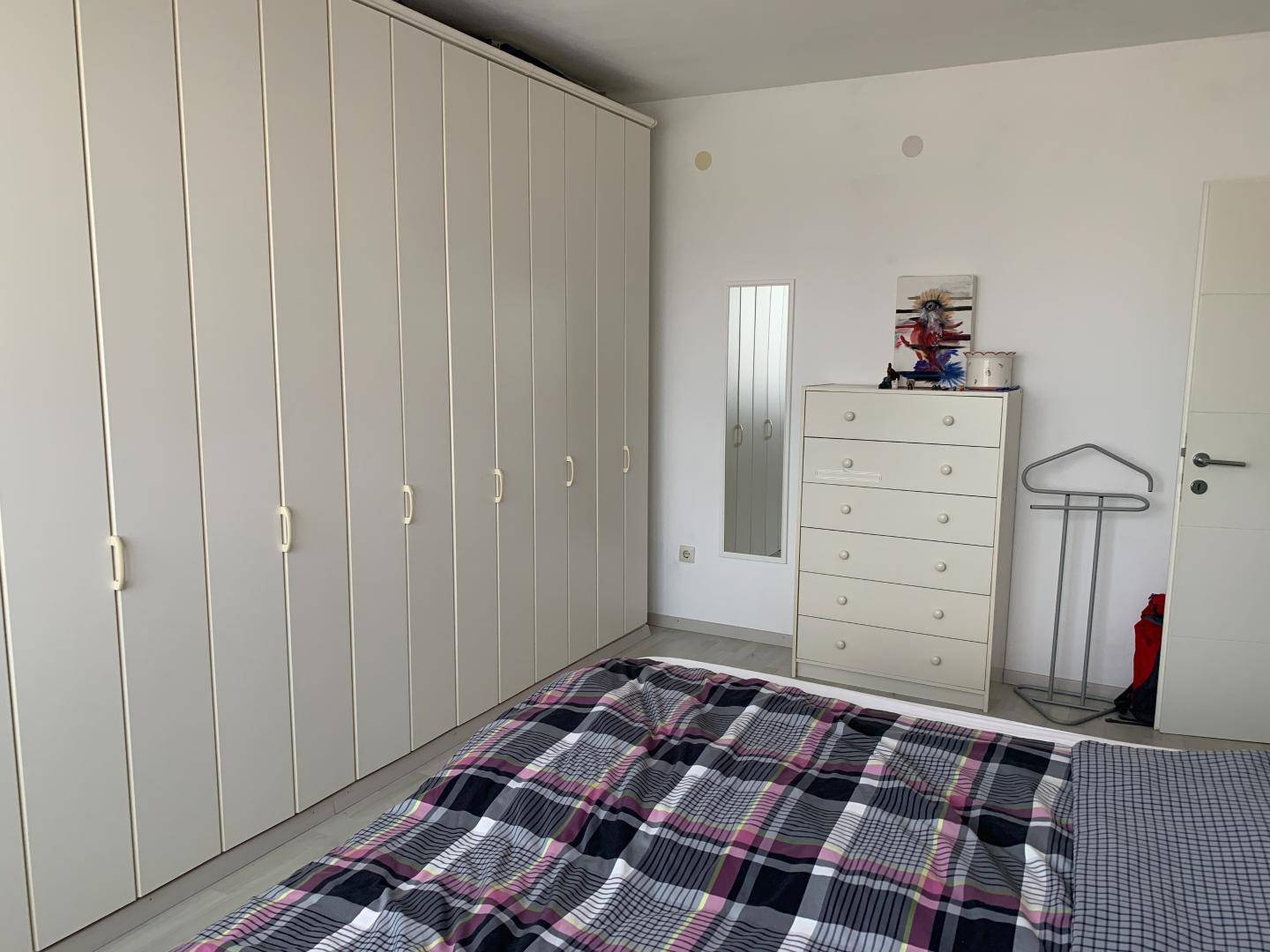 Schlafzimmer mit geräumigen weißen Einbauschränken und einem Bett mit karierter Decke.