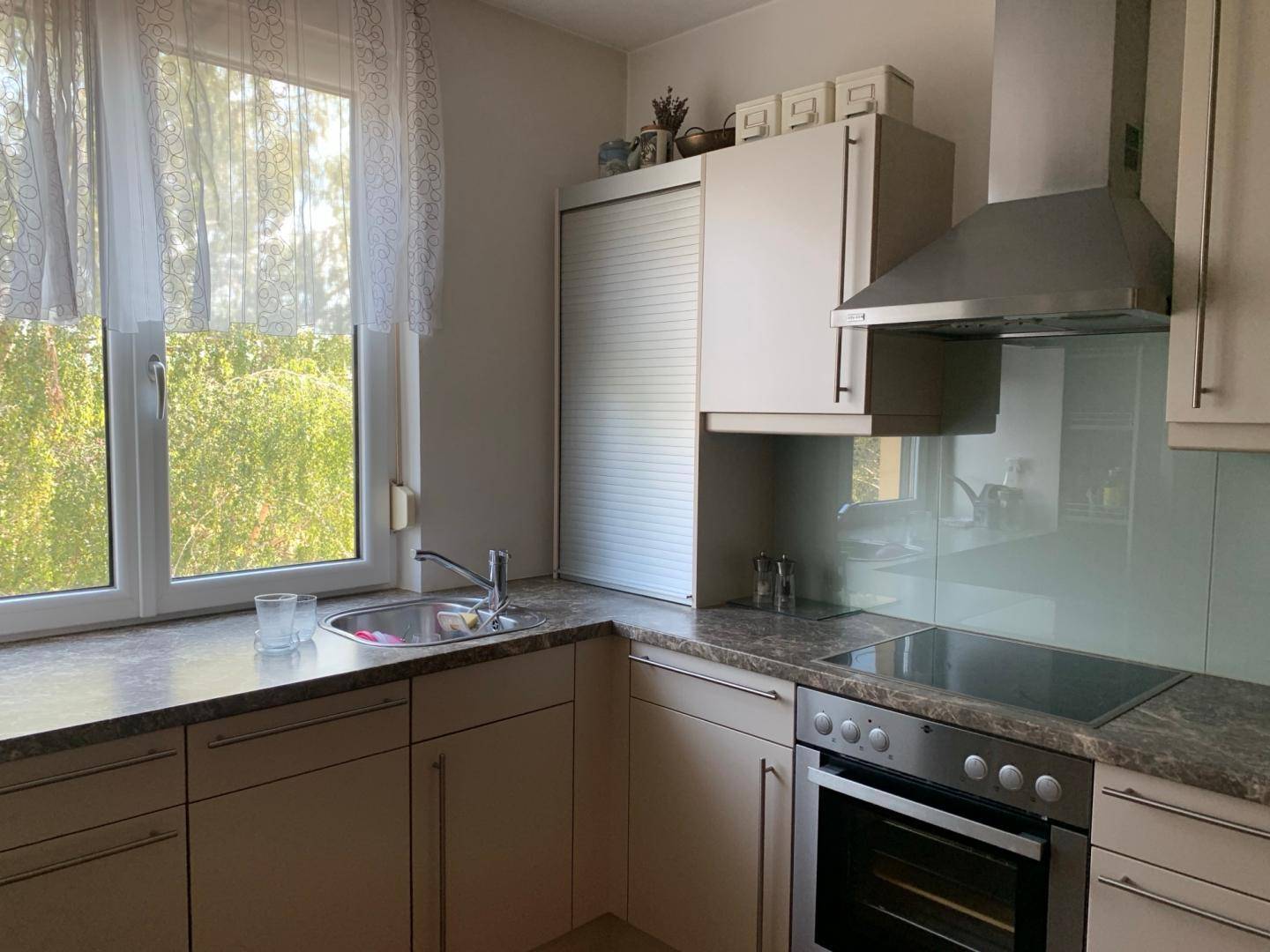 Detailansicht der Küche mit Spüle unter dem Fenster, Kochfeld und Dunstabzugshaube.