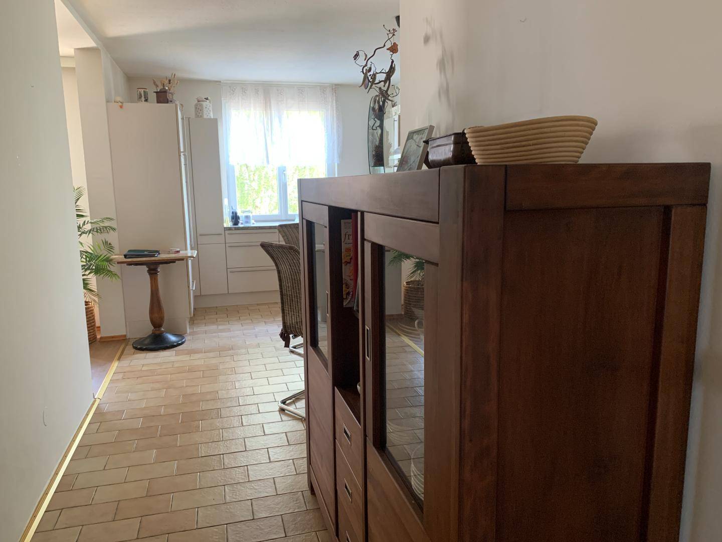 Flur mit Fliesenboden und einem Holzschrank, der zur Küche führt.