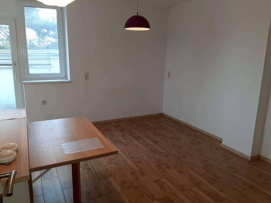 Leerer Essbereich mit Laminatboden und weißen Wänden, beleuchtet durch ein großes Fenster.