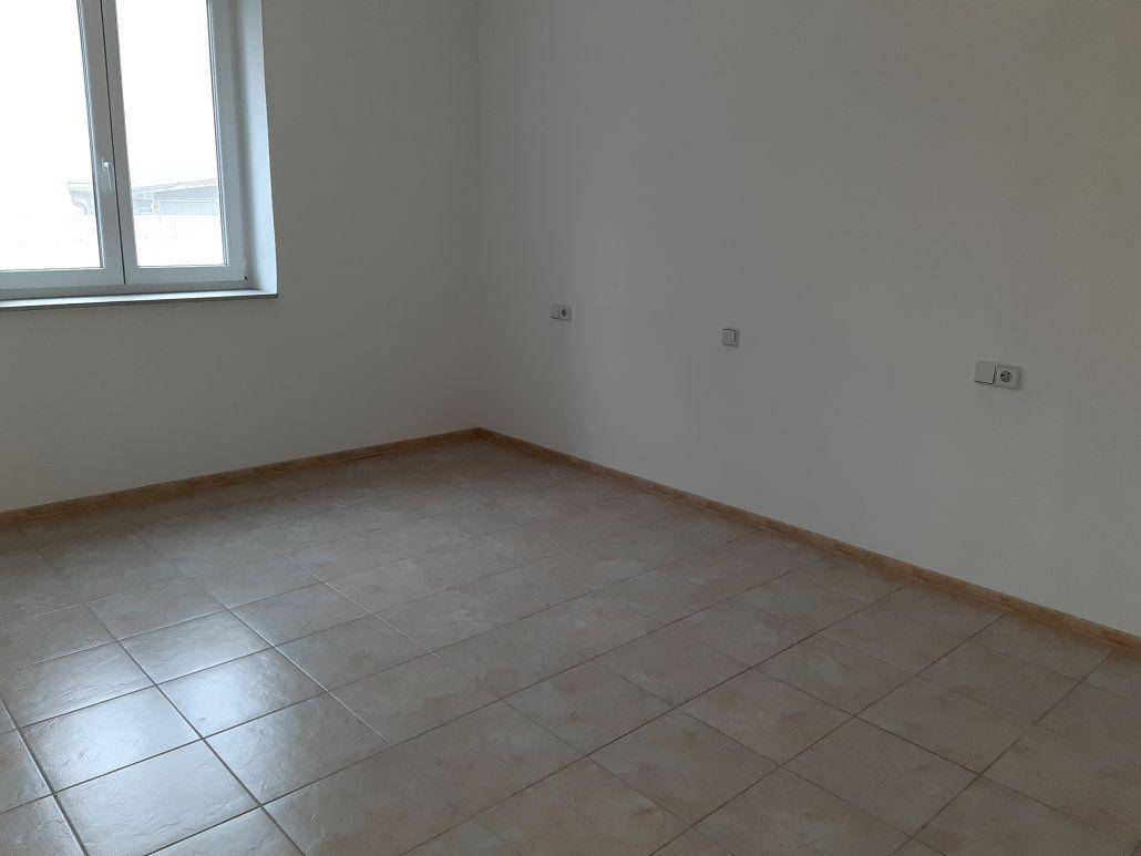 Leerer Raum mit beigefarbenen Fliesen und weißen Wänden, der durch ein Fenster natürliches Licht erhält.