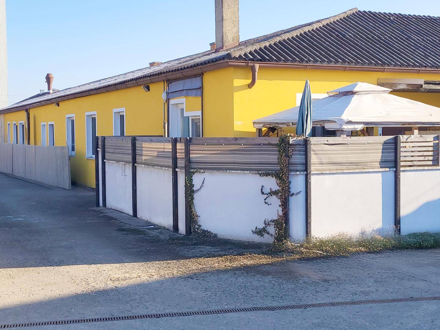 Gelbes Gebäude mit einem umzäunten Bereich, der eine weiße Gartenlaube und eine kleine Terrasse umfasst.