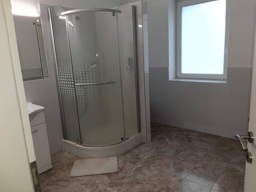 Badezimmer mit einer Eckduschkabine, weißen Fliesen an den Wänden und einem Fenster mit Milchglas.