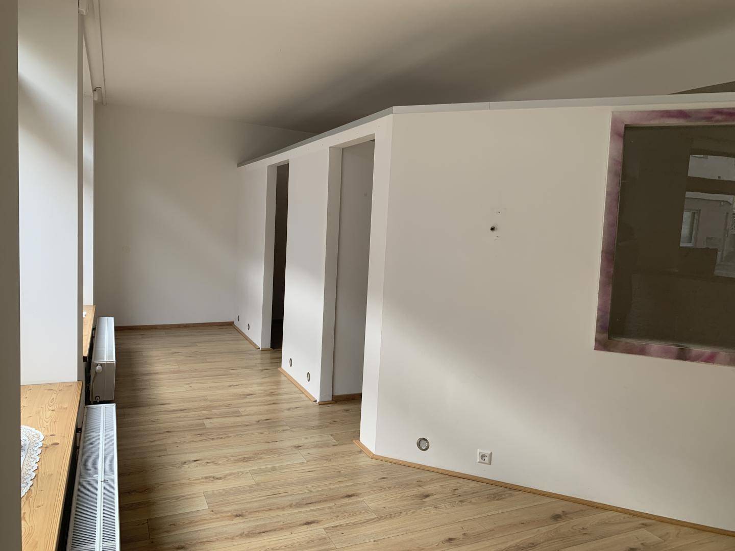 Geräumiger, leerer Raum mit Laminatboden und mehreren Türöffnungen.