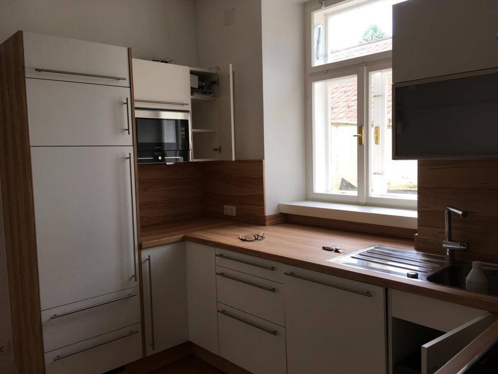 Moderne Küche mit weißen Schränken, Holzarbeitsplatte, Spüle und eingebauter Mikrowelle.