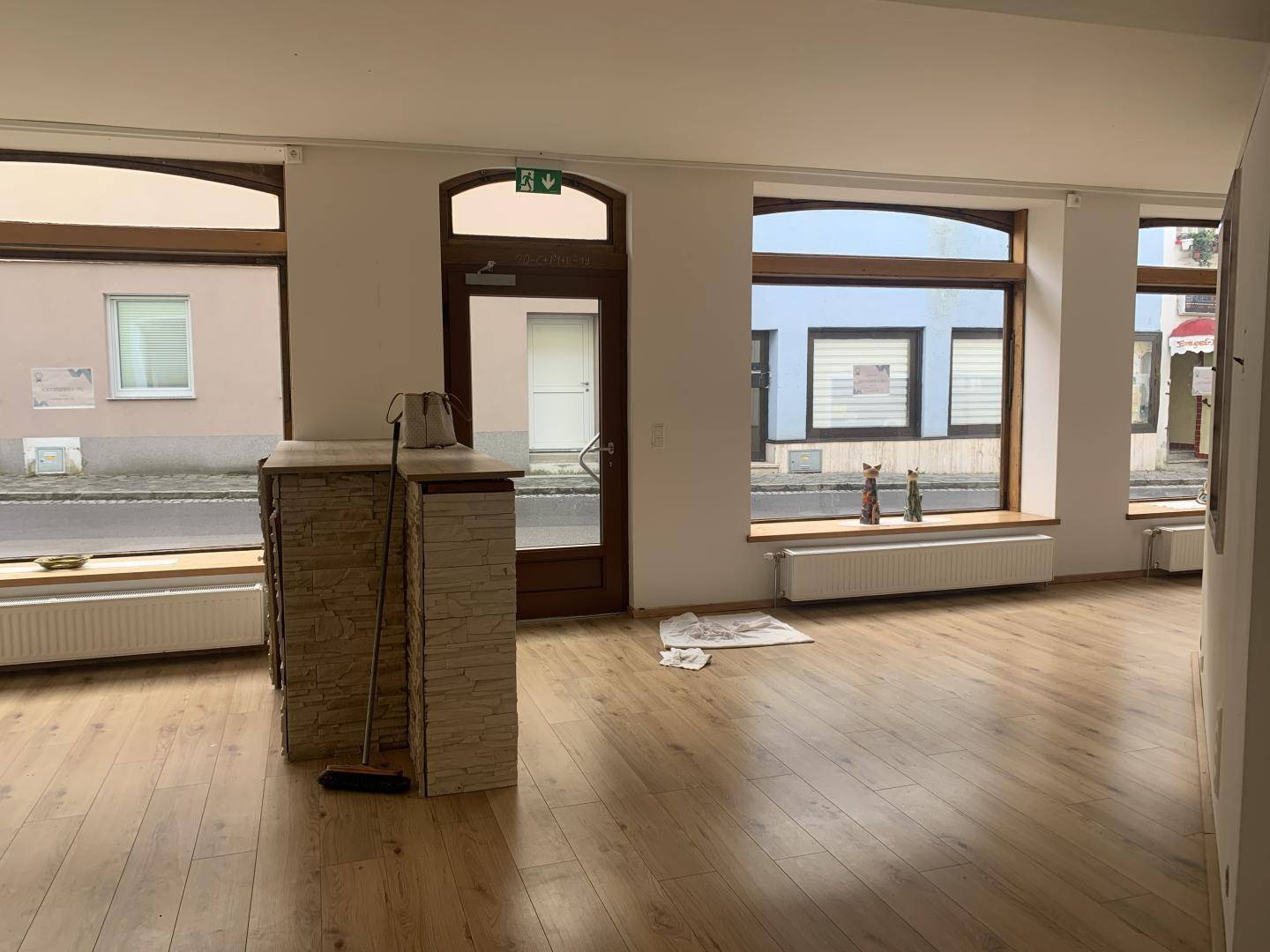 Großer, heller Raum mit Laminatboden, großen Schaufenstern zur Straße und einer Theke.