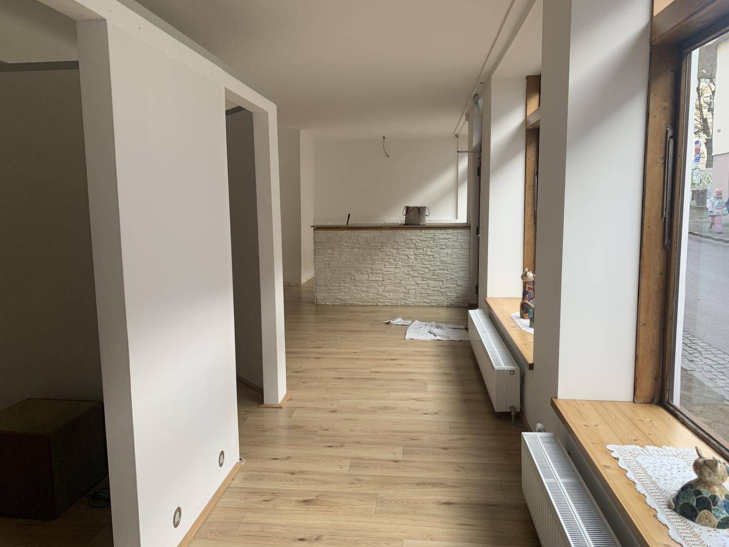 Großer, heller Raum mit Laminatboden, großen Fenstern und einer Theke mit Steinverkleidung.