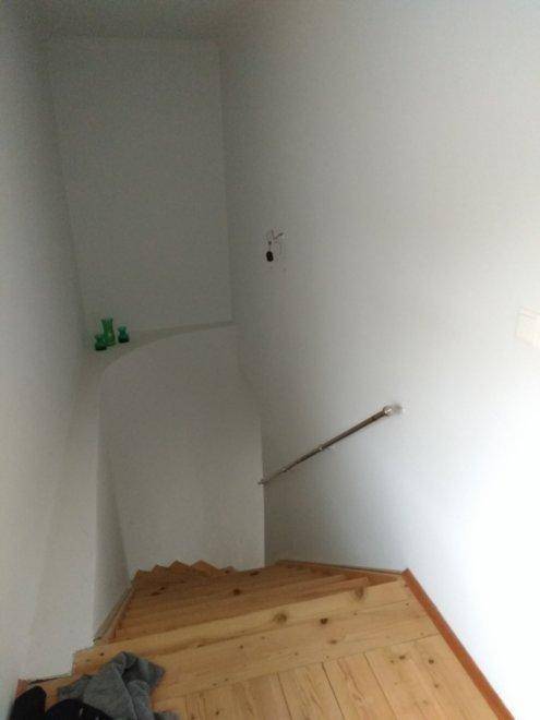 Holztreppe mit weiß gestrichenen Wänden und einem Handlauf, der nach unten führt.