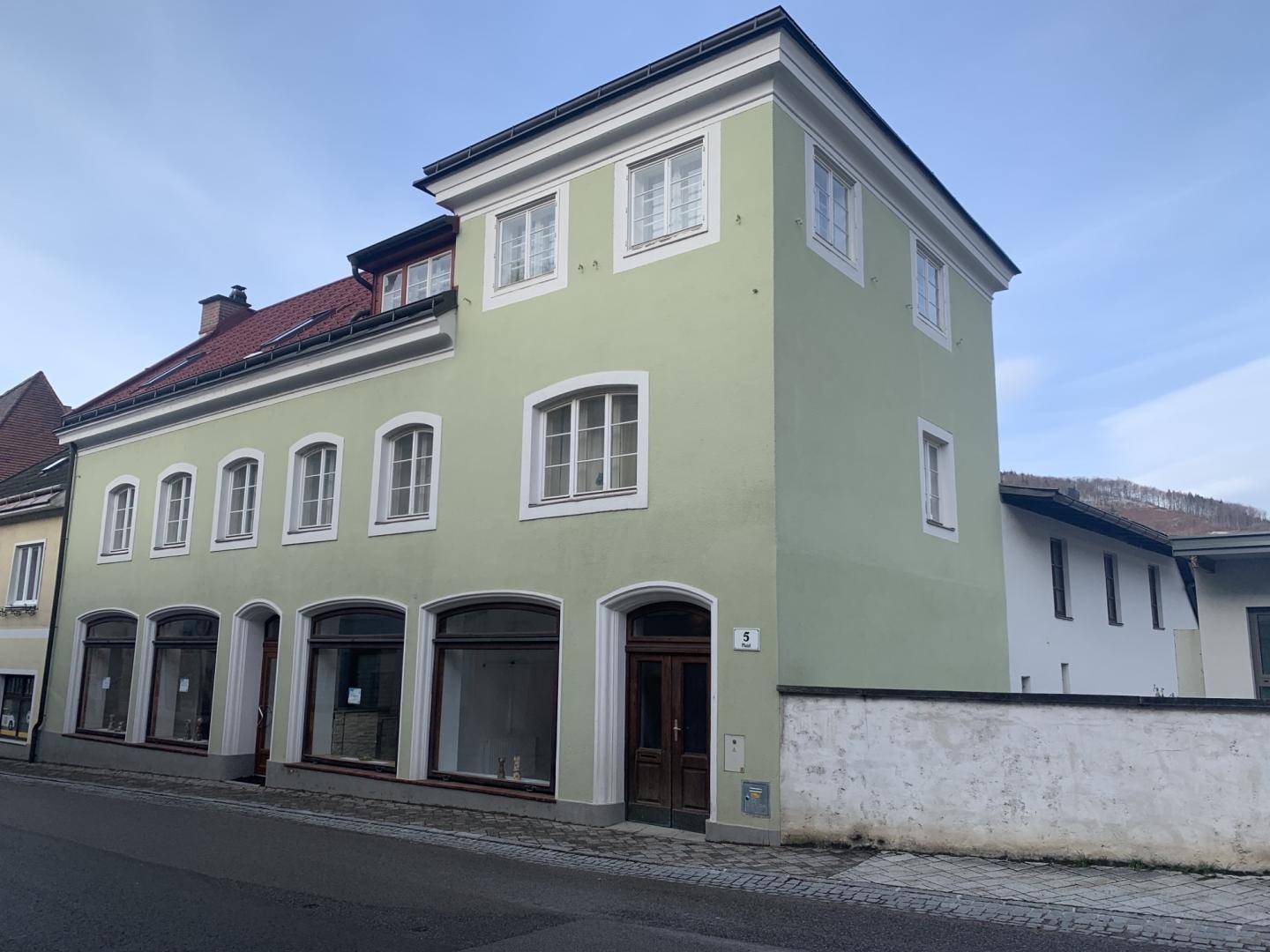 Historisches Gebäude mit hellgrüner Fassade und großen Schaufenstern an einer Straße gelegen.