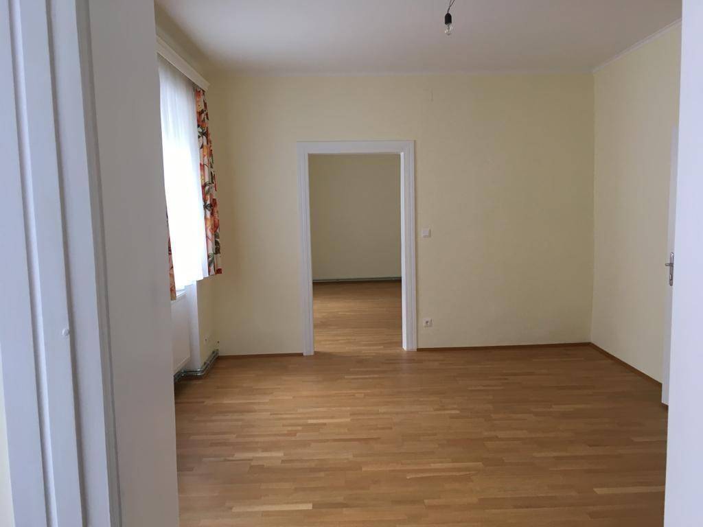 Helles, leeres Zimmer mit Parkettboden und einem Durchgang zu einem weiteren Raum.
