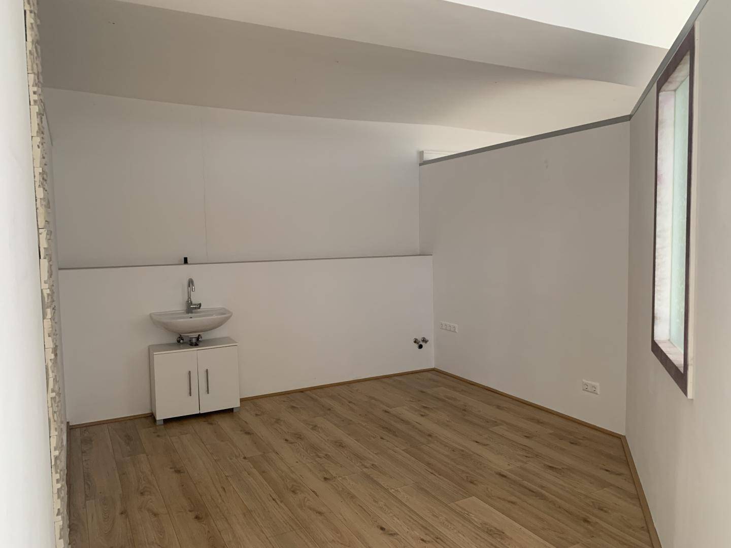 Leerer Raum mit Laminatboden, Fenster und einem kleinen Waschbecken mit Unterschrank.