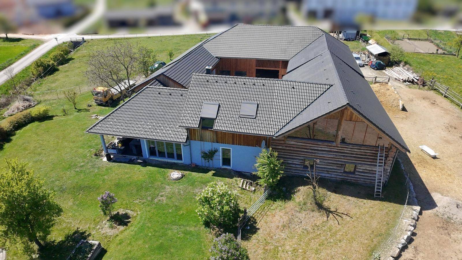 Weitläufige Luftaufnahme des Gebäudes mit Holzfassade und angrenzenden Feldern unter blauem Himmel.