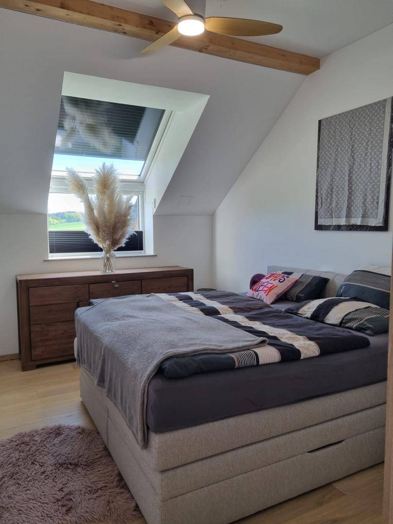 Helles Schlafzimmer mit großem Bett, Holzkommode und Dachfenster in der Dachschräge.