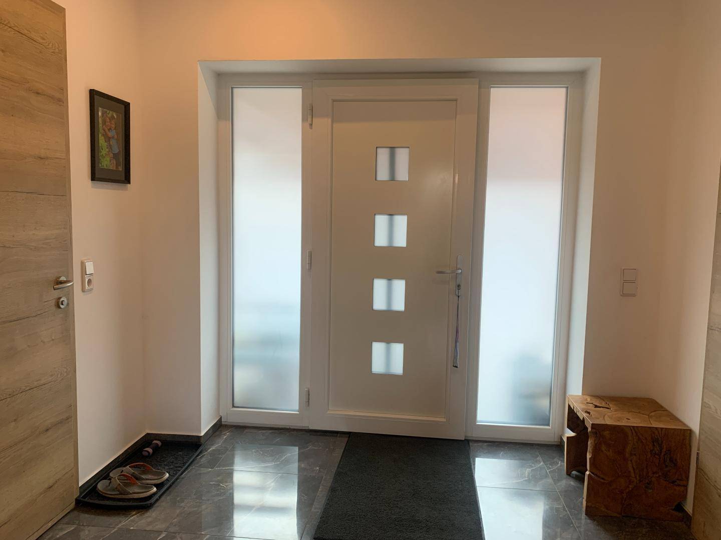 Heller Eingangsbereich mit moderner weißer Tür, Milchglas-Seitenteilen und dunklem Fliesenboden.