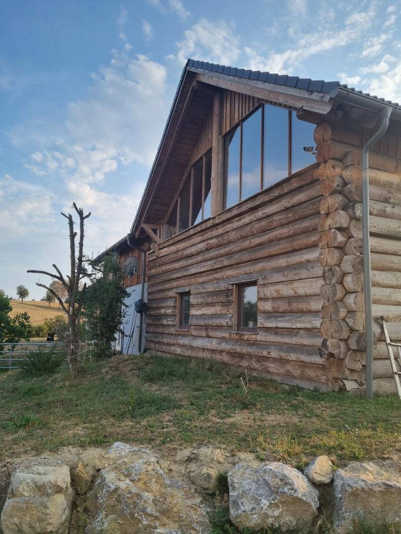 Seitenansicht des Holzblockhauses mit sichtbaren Baumstämmen und großen Fensterflächen.