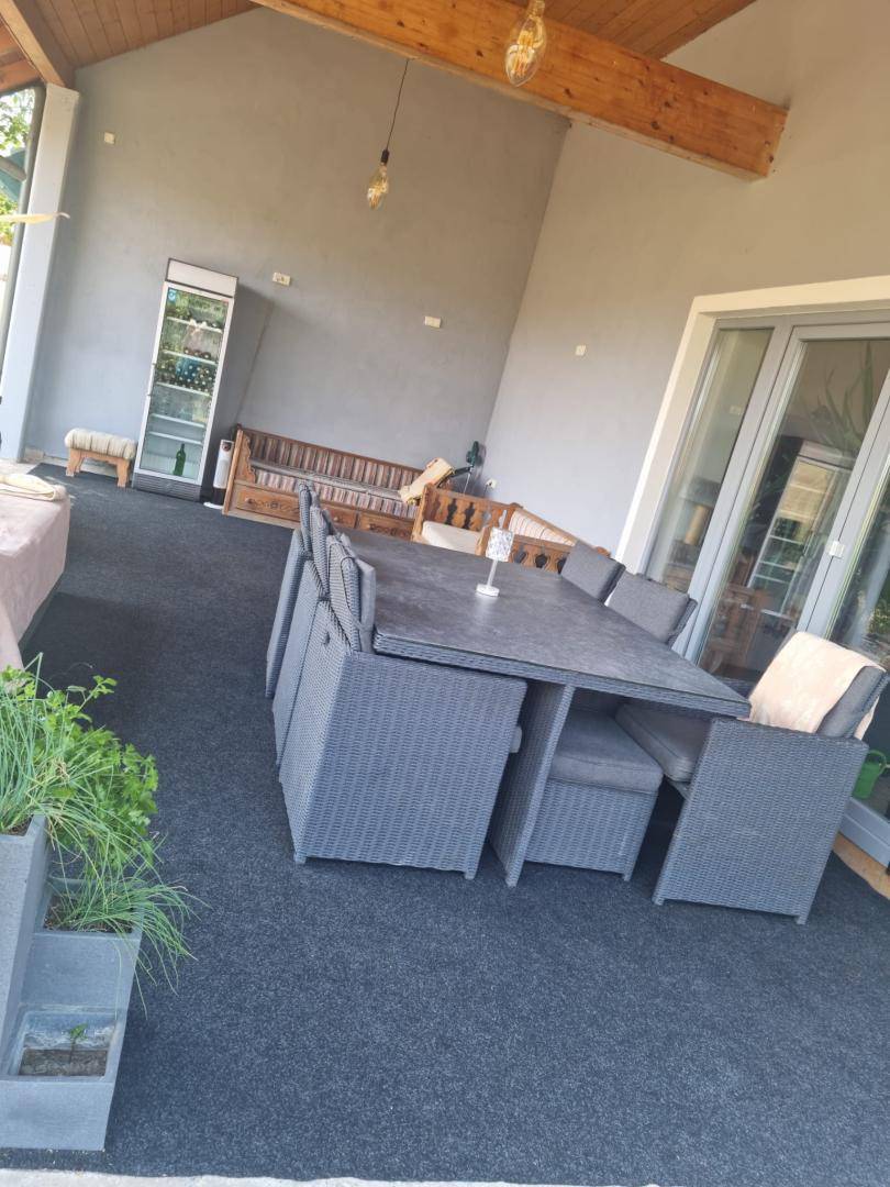 Überdachte Terrasse mit großem Esstisch, bequemen Sitzgelegenheiten und Getränkekühlschrank.
