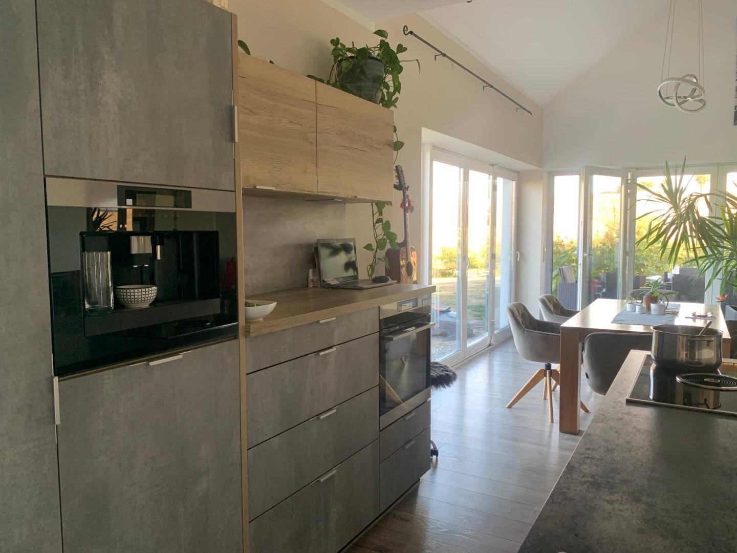 Moderne Küche mit grauen Fronten, Holzakzenten und integrierter Kaffeemaschine, offen zum Essbereich.