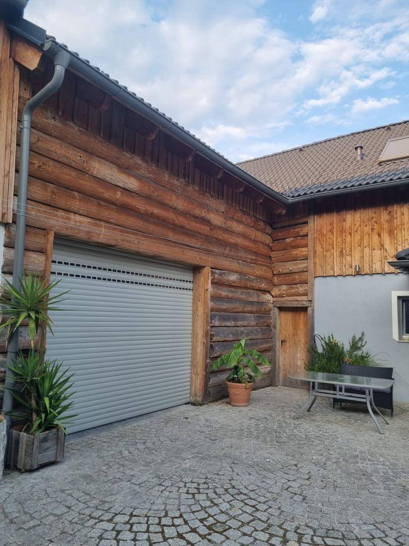 Eingangsbereich des Holzblockhauses mit Garagentor und gepflastertem Hofbereich.