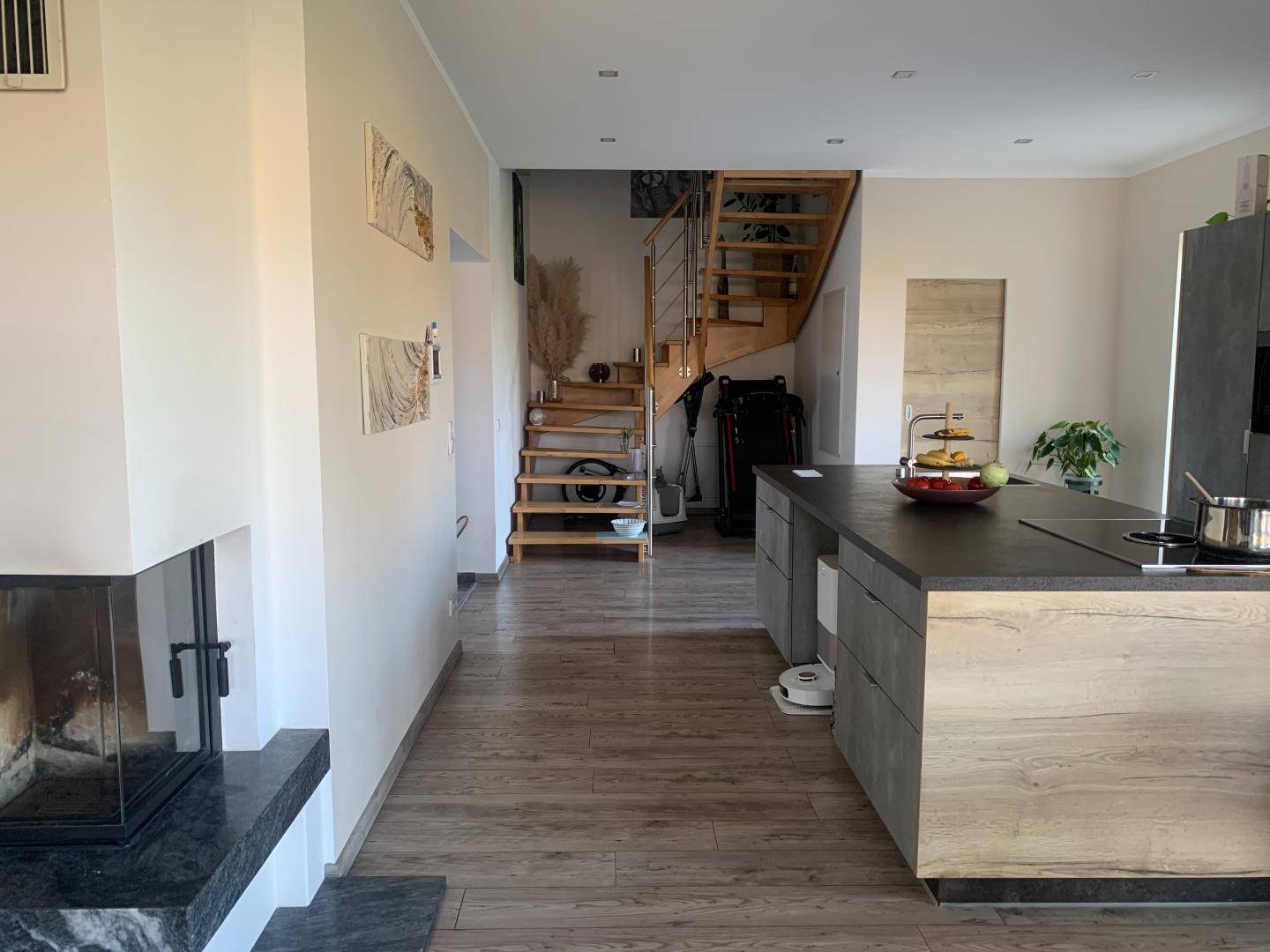 Offener Wohnbereich mit Kamin, Kücheninsel und eleganter Holztreppe, die in die obere Etage führt.