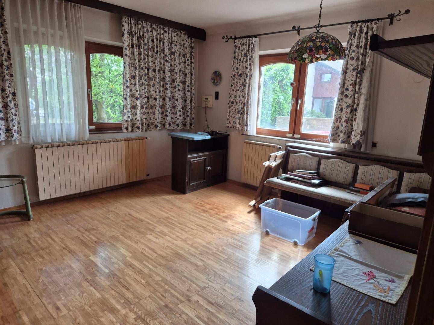 Heller Wohnraum mit Holzparkettboden, traditionellen Möbeln und Fenstern mit Vorhängen.