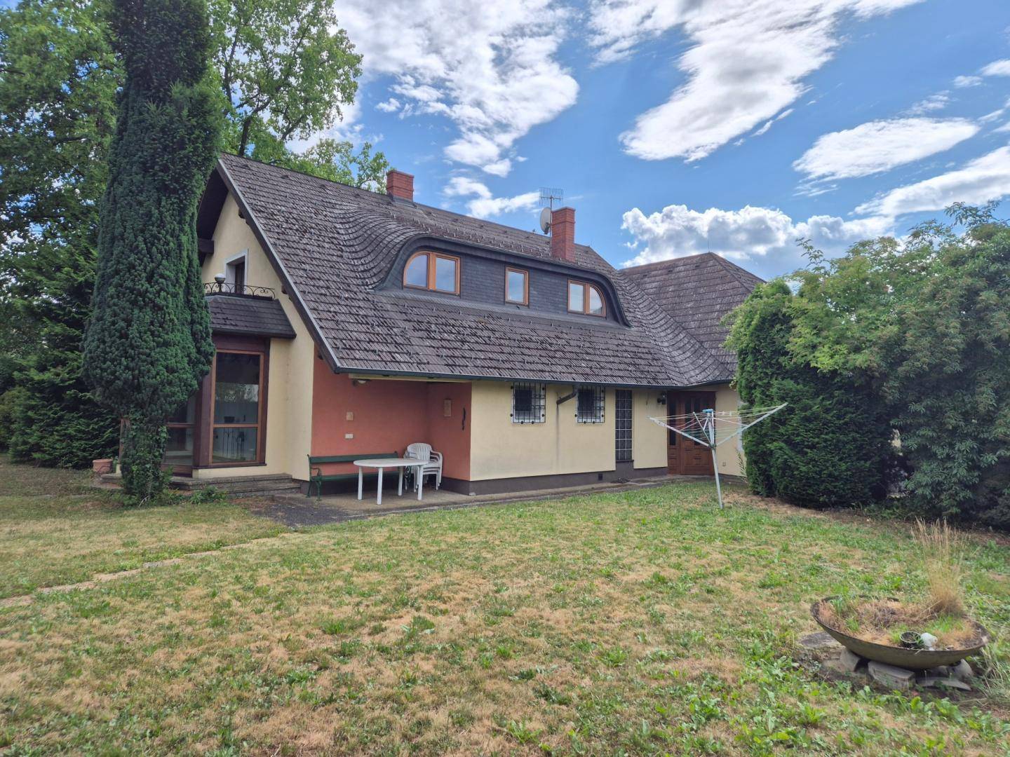 Rückansicht des Hauses mit kleiner Terrasse und Wäscheleine, umgeben von einem grünen Garten.
