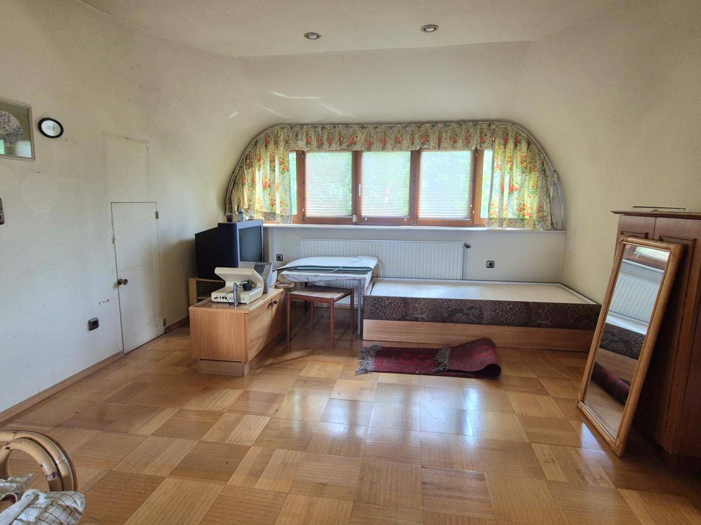 Schlafzimmer im Dachgeschoss mit Dachschräge, Holzparkett und einem breiten Fenster.