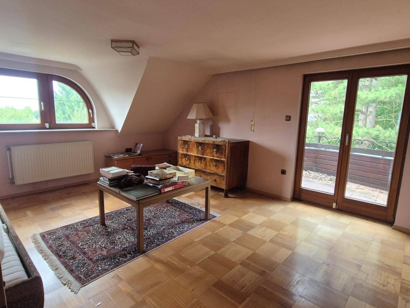 Dachgeschosszimmer mit Holzparkett, Dachschräge und Zugang zu einem kleinen Balkon.