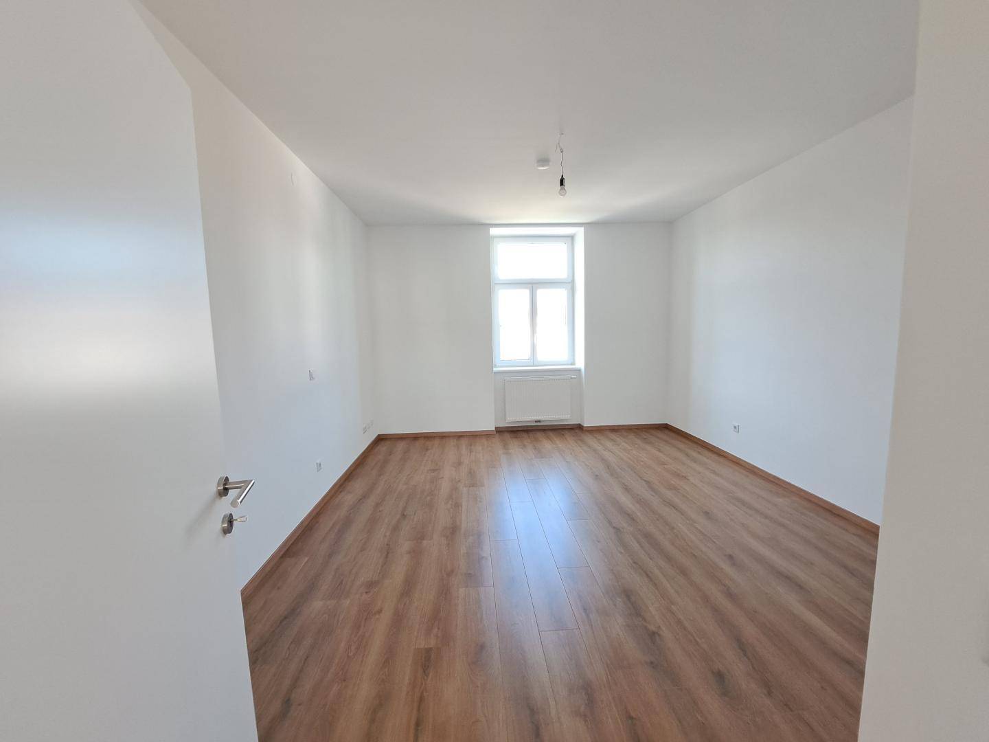 Leerer, heller Raum mit Laminatboden und einem einzelnen Fenster, bereit zur individuellen Gestaltung.