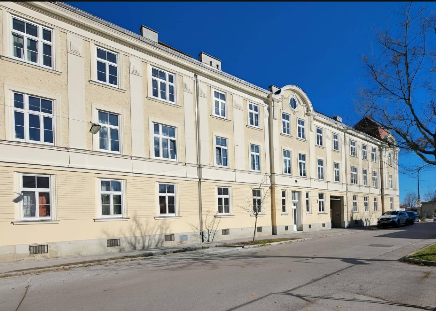 Klassisches Mehrfamilienhaus mit vielen Fenstern und einer hellen Fassade an einer ruhigen Straße.
