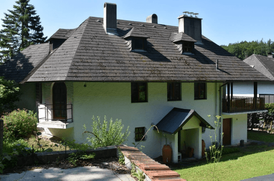 Seitenansicht des Hauses mit mehreren Balkonen und einem markanten Dach mit Gauben.