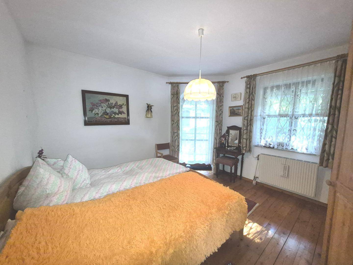 Helles Schlafzimmer mit Doppelbett, Holzboden und zwei Fenstern mit Blick ins Grüne.