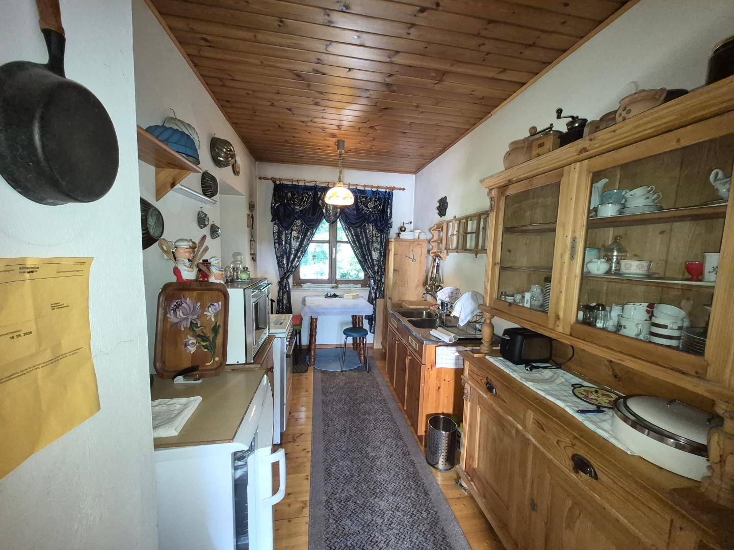 Rustikale Küche mit Holzschränken, Holzbalkendecke und einem kleinen Essbereich am Fenster.