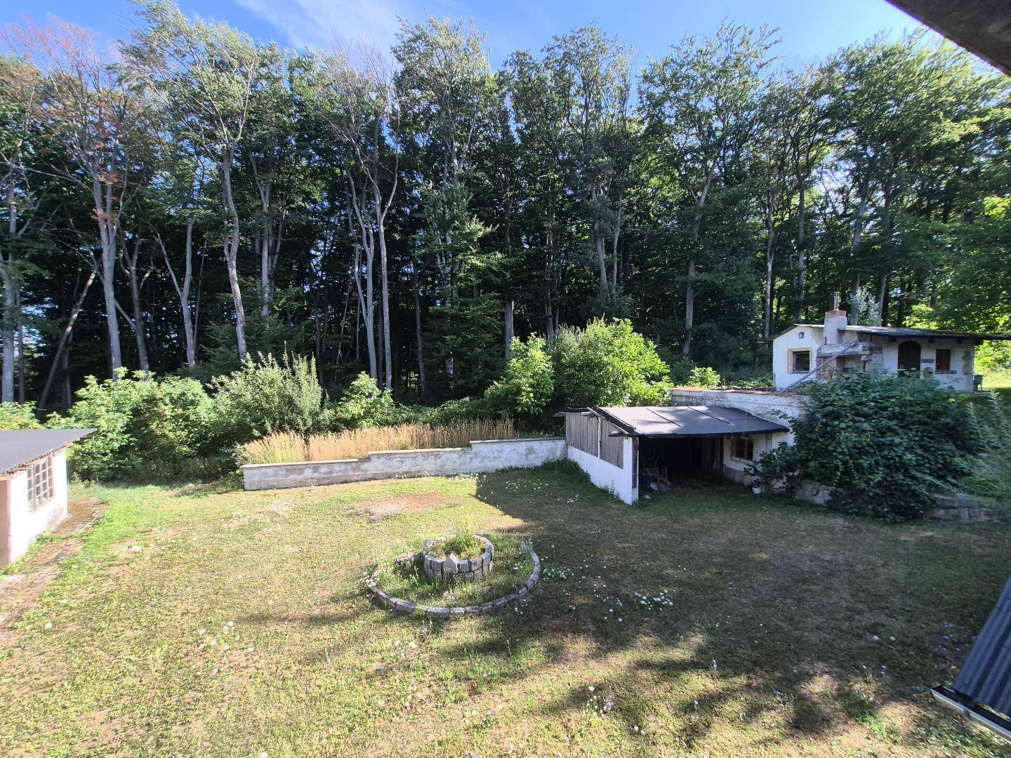 Weitläufiger Gartenbereich mit Nebengebäuden, einer Feuerstelle und dichtem Baumbestand.