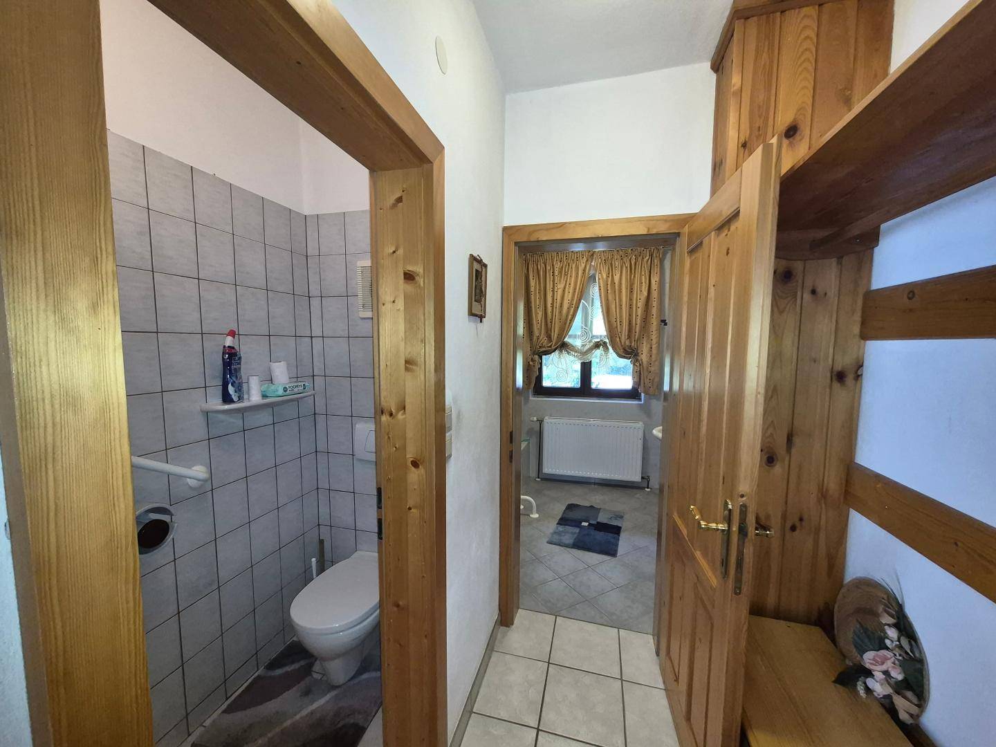 Kleines WC mit gefliesten Wänden, Haltegriffen und einer Holzablage im Eingangsbereich.