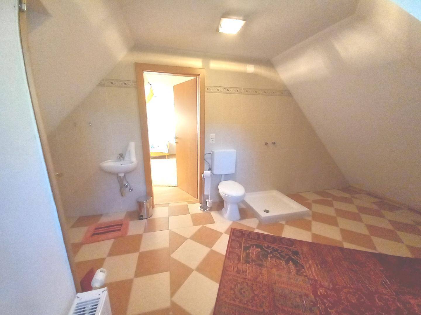 Badezimmer im Dachgeschoss mit schrägen Wänden, Waschbecken und Toilette, gefliester Boden.