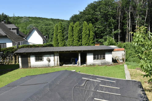 Blick auf ein Nebengebäude mit Garage und Rasenfläche, umgeben von Bäumen und weiteren Häusern.