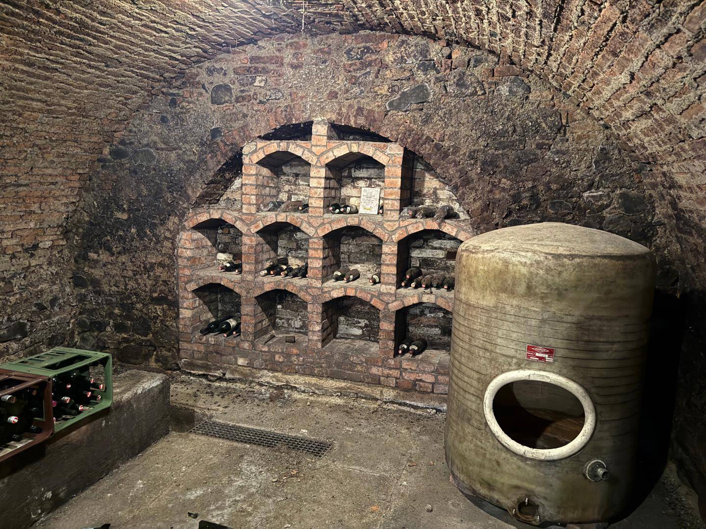 Historischer Weinkeller mit Ziegelgewölbe, eingebauten Weinregalen und großem Tank.