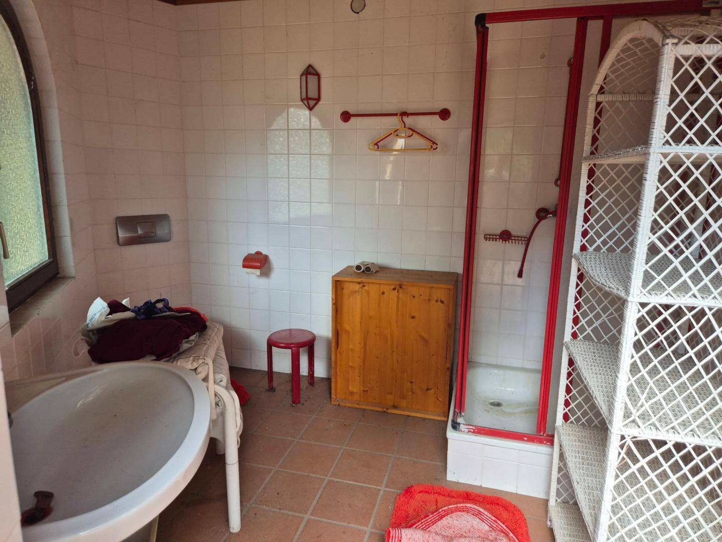 Badezimmer mit weißen Fliesen, Waschbecken und Duschkabine in älterem Zustand.