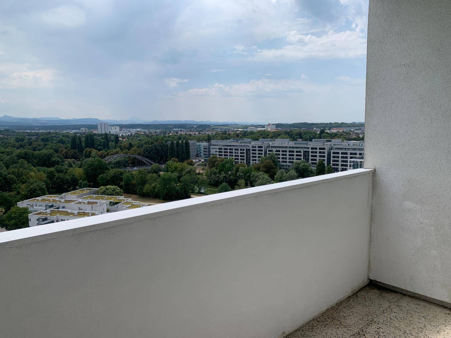 Balkon mit weitem Blick über die Stadt und grüne Landschaften unter bewölktem Himmel.