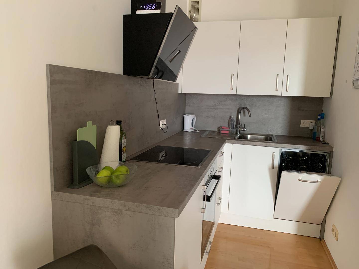 Kompakte Küche mit integriertem Geschirrspüler, weißen Schränken und grauer Arbeitsfläche.