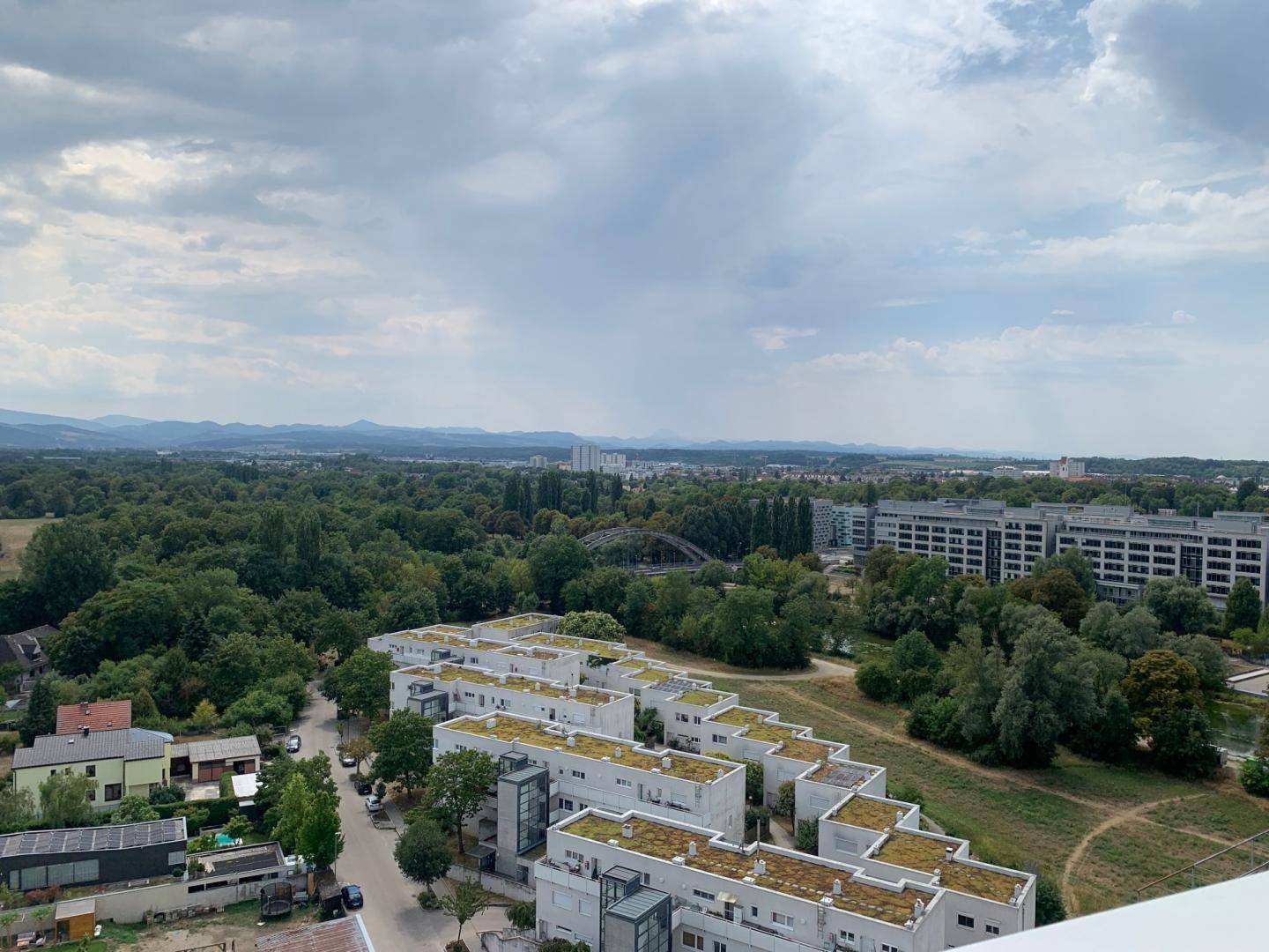 Panoramablick von oben über eine Wohnsiedlung mit viel Grün und Bergen im Hintergrund.