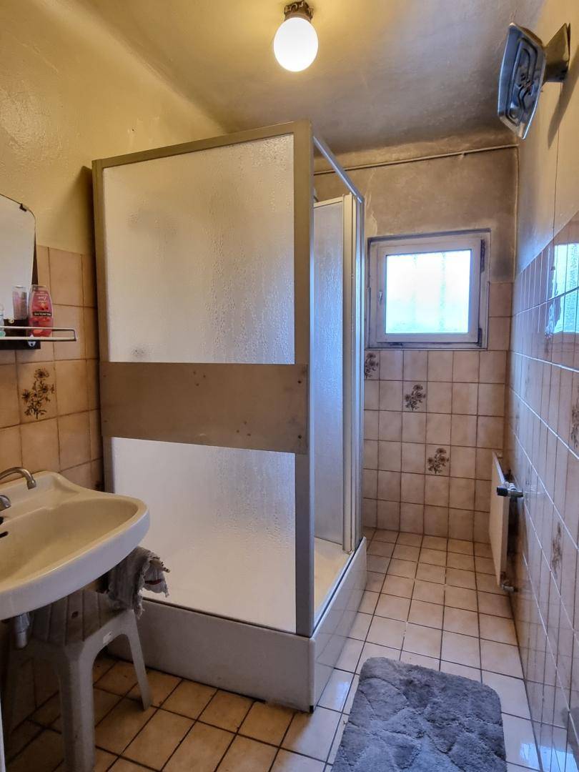 Badezimmer mit Duschkabine, Waschbecken und gefliesten Wänden und Boden in älterem Stil.