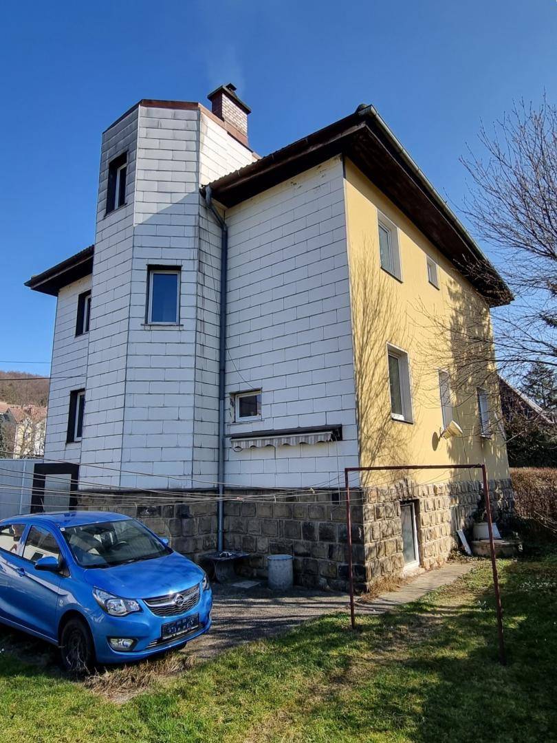 Seitenansicht des Hauses mit gelber Fassade, Steinsockel und einem geparkten blauen Auto.