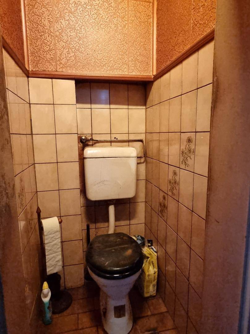 Kleines WC mit beigefarbenen Fliesen und älterer Toilette in originalem, funktionalem Zustand.