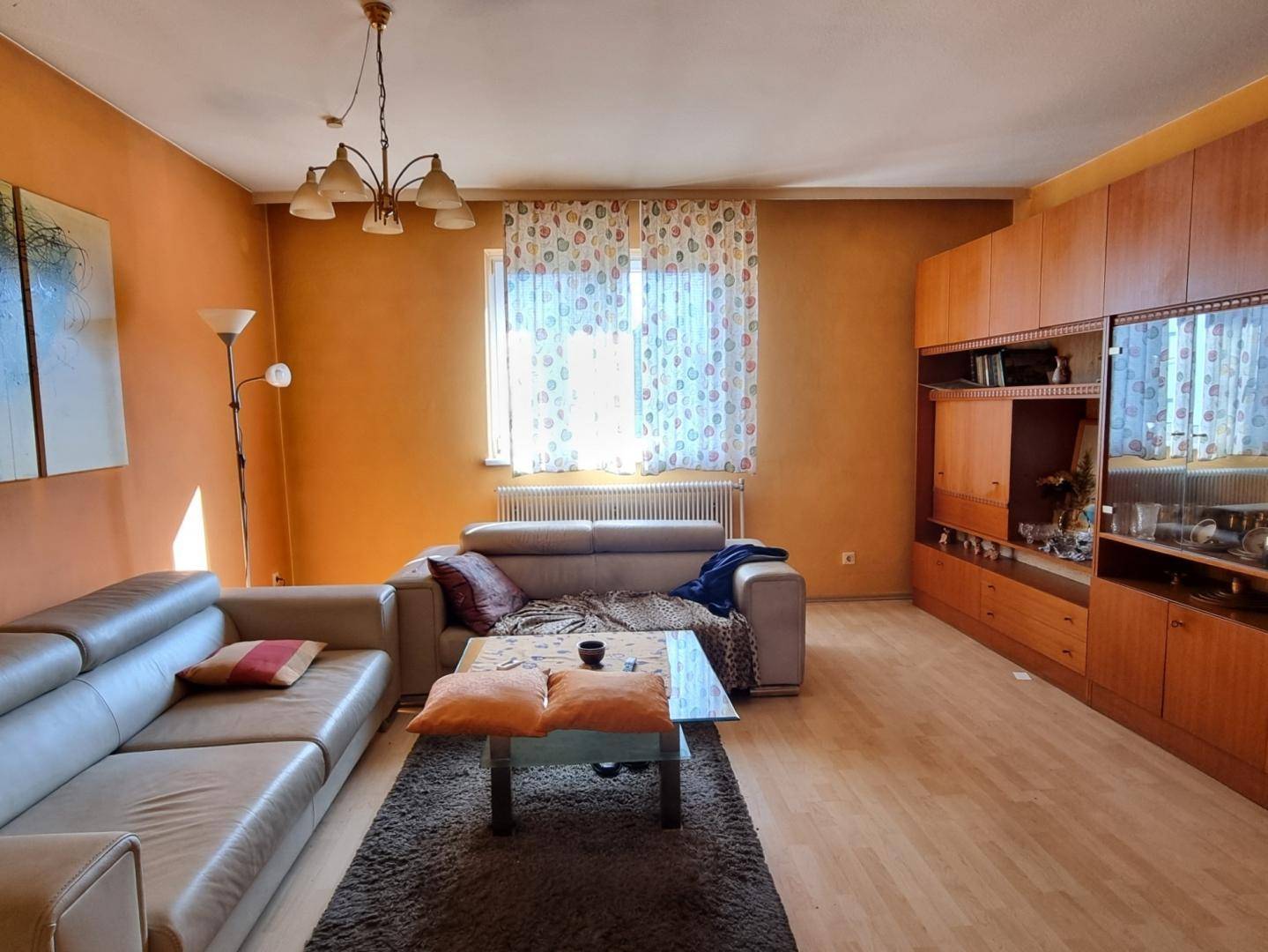 Geräumiges Wohnzimmer mit Sofa, Couchtisch und großer Schrankwand in warmen Farbtönen.